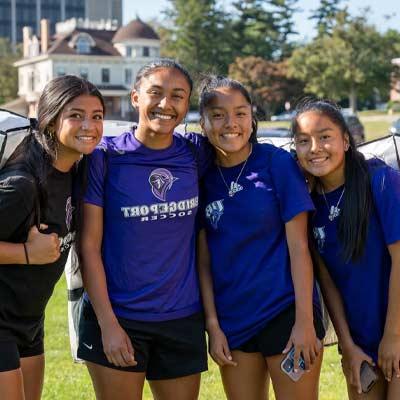 group of 4 smiling students carrying duffle bags